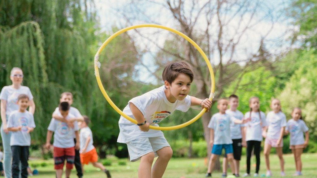 a young boy holding a yellow hula hoop in front of a group of people